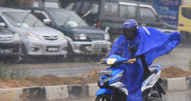 Tampak pengendara motor menggunakan mantel melintas.