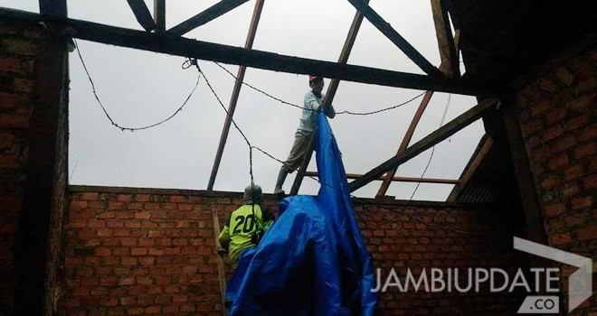 Terlihat warga yang memperbaiki atap rumah yang rusak akibat angin puting beliung.
