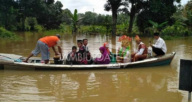Terlihat pasangan pengantin saat dievakuasi menggunakan perahu karena lokasi pelamainan terkena banjir.