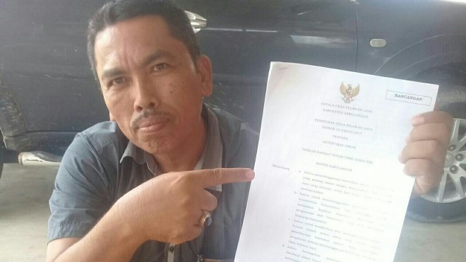 Kades Pelawan Jaya saat memperlihatkan Peraturan Desa.