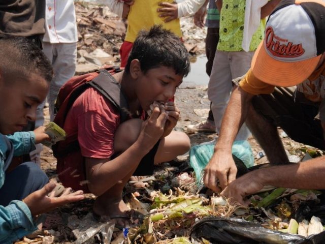 Beberapa tangan kecil menggali ke dalam kantong sampah dan memasukkan isinya ke mulut mereka. Satu potongan tampak seperti sepotong roti yang basah (Sky News)