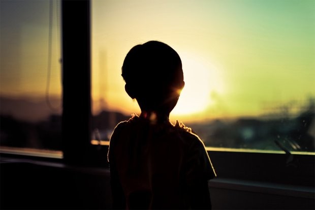 Silhouette of child by window looking at sunset.