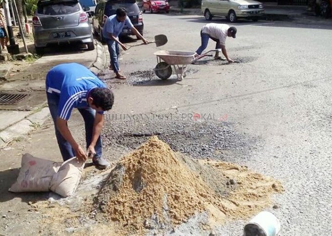 Warga berinisiatif menambal jalan yang rusak.
