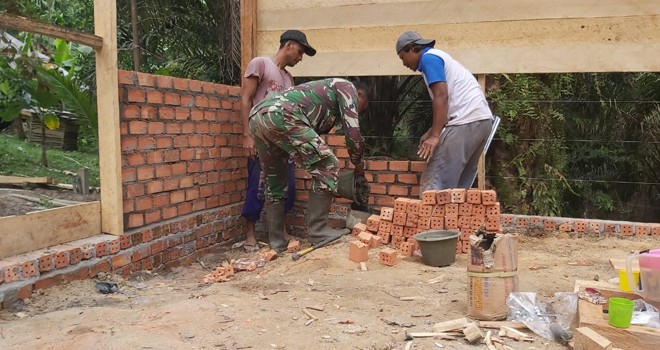 Sertu Bambag Sutomo Babinsa Koramil 415-04/MB membantu warga gotong royong memasang batu-bata dinding rumah milik Marlan RT 05, Desa Ladang Peris, Kecamatan Bajubang, Kabupaten Batanghari.