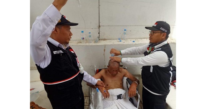 KELELAHAN: Petugas dari PPIH Arab Saudi mengguyur kepala Upah Supandi dengan air mineral. (HILMI SETIAWAN/JAWA POS)