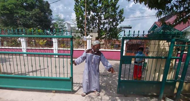 Sudarno bersama cucu laki-lakinya menunjukkan pintu pagar masjid. 