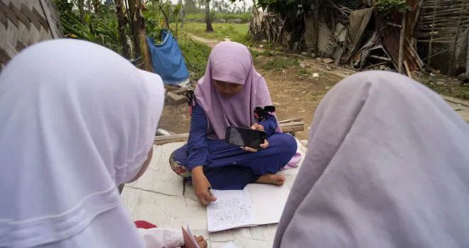 Tiga siswi melakukan belajar bersama di depan halaman rumah yang terlihat tak layak para siswi sekolah dasar giat melakukan belajar dengan bergantian menggunakan telepon selular (belajar daring), sebagian besar siswa kelas satu tidak memiliki alat komunikasi telepon pintar sebagai pendukung belajar secara daring, Kabupaten Tangerang, Banten. (26/7). FOTO: FAISAL R. SYAM / FAJAR INDONESIA NETWORK.